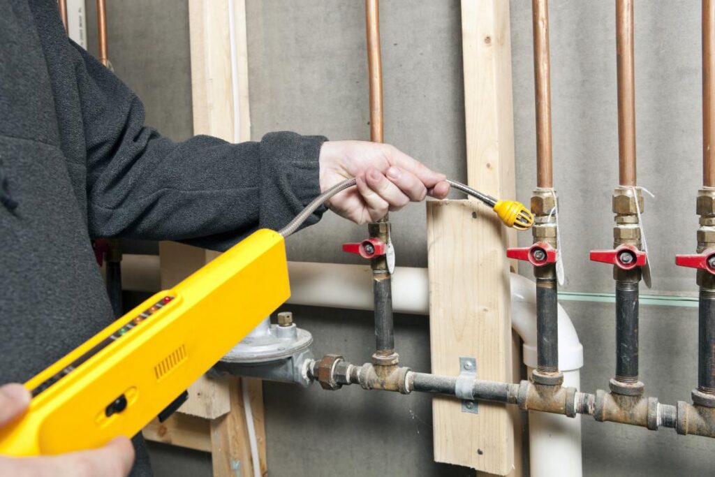 Technician using a gas leak detector on piping